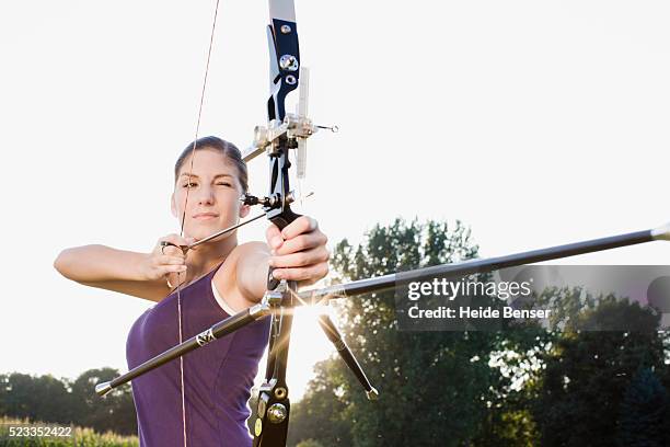 young woman aiming a bow and arrow - tiro con l'arco foto e immagini stock