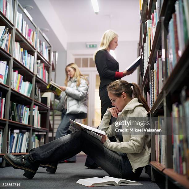 Students Using Library Female University Student Sitting On A Library Floor Reading A Book ...