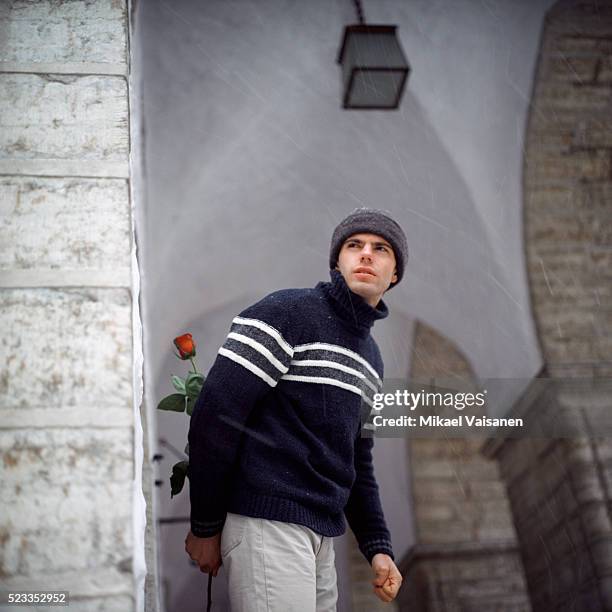 young man with rose behind his back keeping a lookout - impatience flowers stock-fotos und bilder