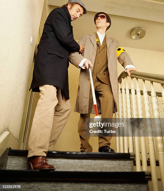 blind man walking down stairs with the aid of a man - オーバーコート ストックフォトと画像