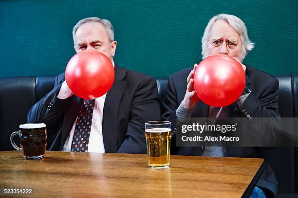 senior man sitting in pub and blowing up balloons - altbier stock-fotos und bilder