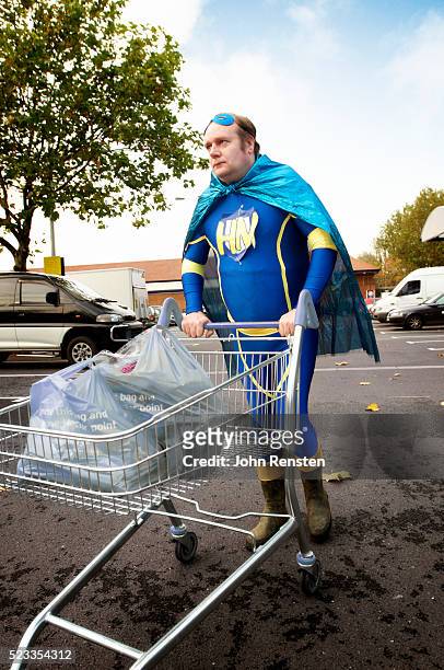 man in superhero costume pushing grocery cart - chubby man shopping stock-fotos und bilder