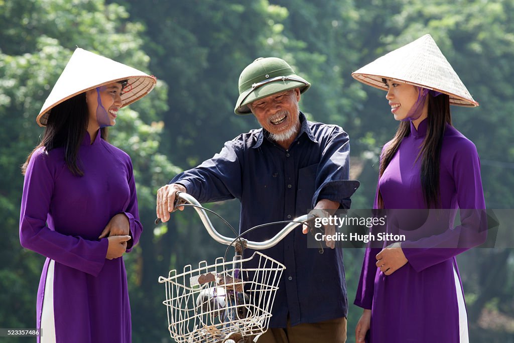 Vietnamese women talking to older man with bicycle. Vietnam