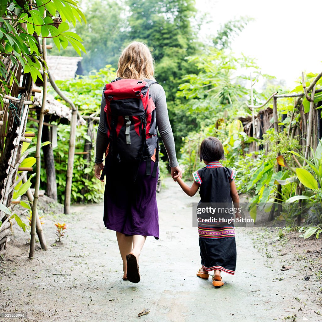Female tourist and local child (4-5) walking through village, Chiang Mai, Thailand