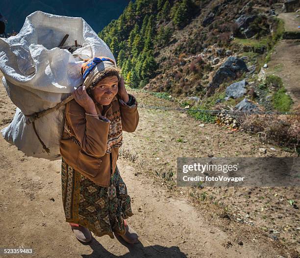 senior sherpa-porter frau mit schwerem gepäck in himalajagebirge nepals - buck teeth stock-fotos und bilder