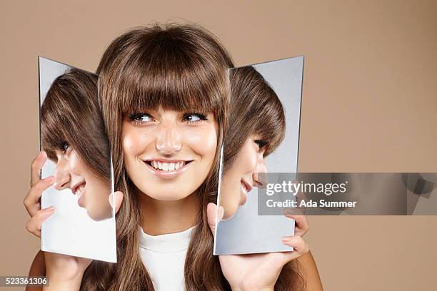 young smiling brunette holding two mirrors to her face - brunette woman foto e immagini stock