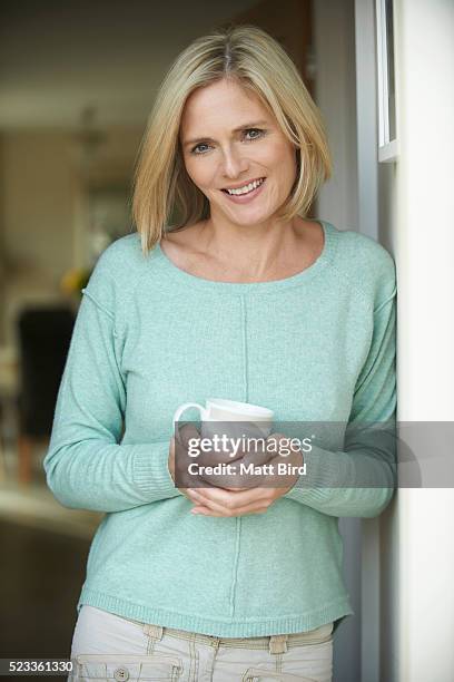 portrait of blonde middle aged woman in doorway holding cup - bob bird stock pictures, royalty-free photos & images