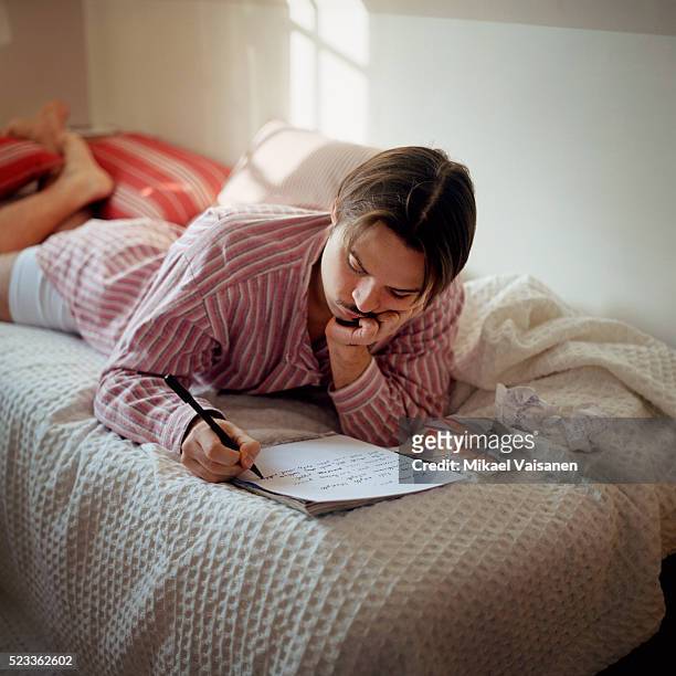 young man lying on bed writing letter - love letter stock-fotos und bilder