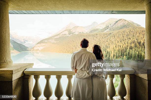 young couple overlooking lake louise on balcony, banff national park, alberta, canada - luna de miel fotografías e imágenes de stock