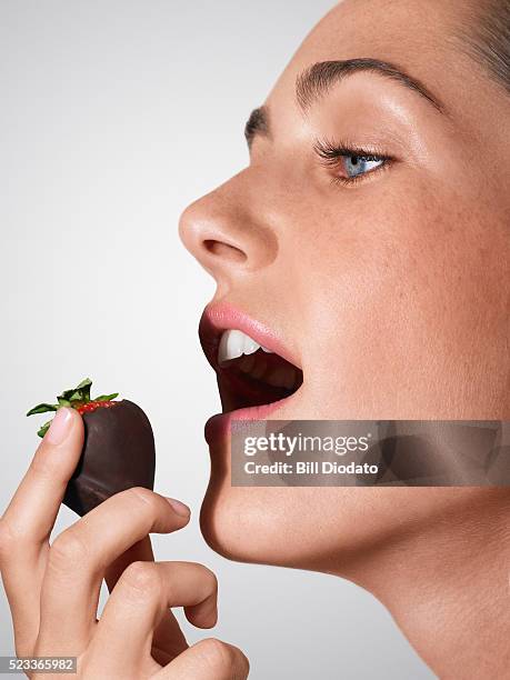 woman eating a chocolate covered strawberry - human mouth stockfoto's en -beelden