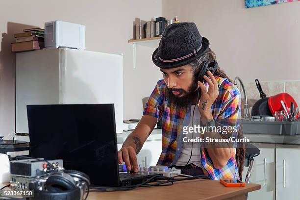 hip hop musician working on laptop at dj table in kitchen - headphones turntable stock-fotos und bilder