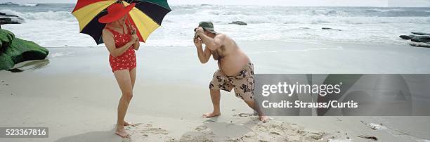 senior couple taking photos on the beach - fat man on beach stockfoto's en -beelden