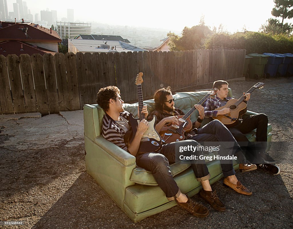 Friends sitting on sofa in backyard playing guitars