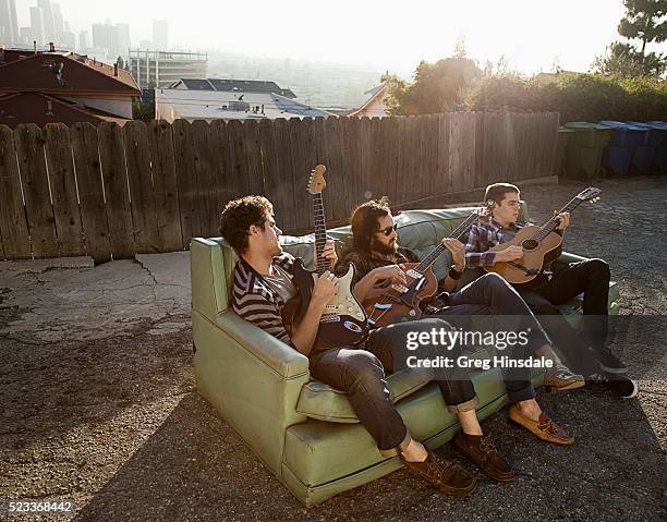 friends sitting on sofa in backyard playing guitars - freunde couch stock-fotos und bilder