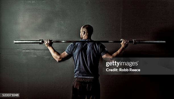 man in gym gym with weight bar on shoulders - over shoulder man stockfoto's en -beelden