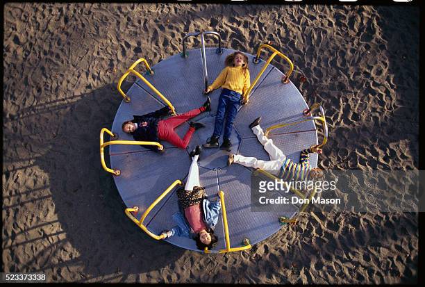 children lying on playground merry-go-round - playground stock pictures, royalty-free photos & images