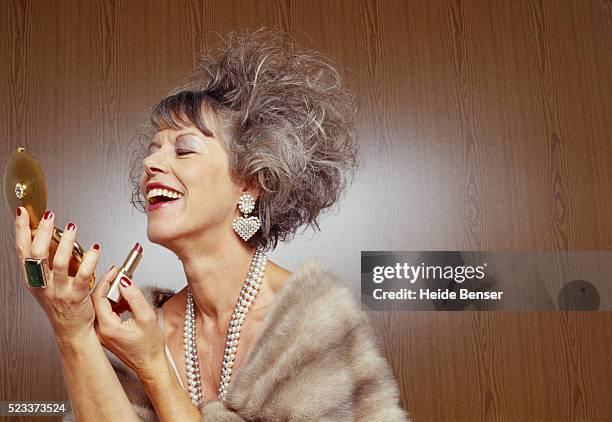 mature woman putting on make-up - símbolo de estatus fotografías e imágenes de stock