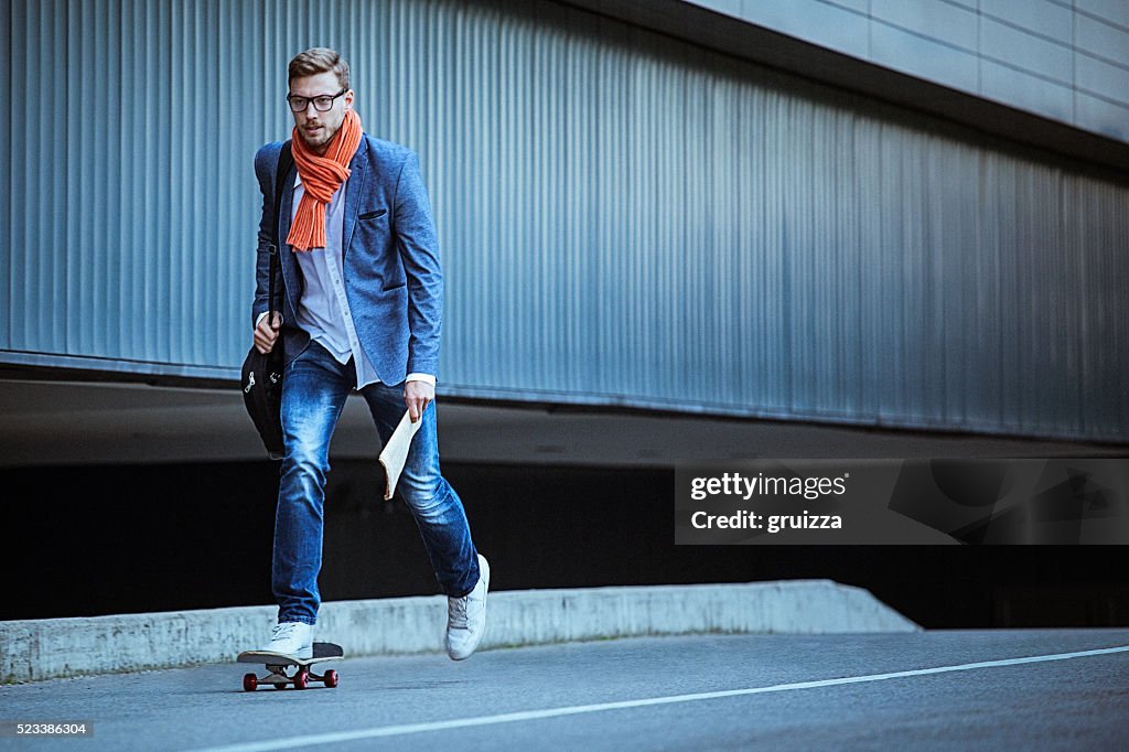 Young casual businessman comuting to work skateboarding.
