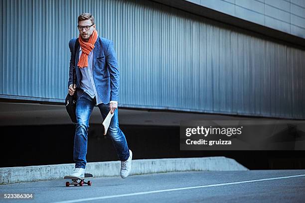 young casual businessman comuting to work skateboarding. - scarf stock pictures, royalty-free photos & images