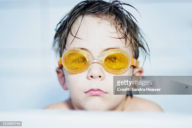 portrait of boy ( 8-9 ) sitting in bathtube with yellow swimming goggles - bathtube stock pictures, royalty-free photos & images