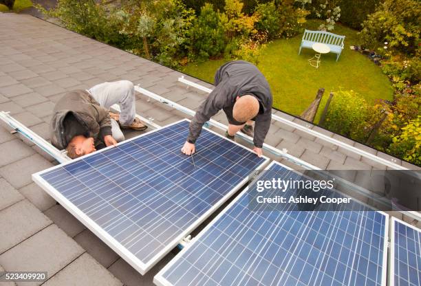 technicians fitting solar photo voltaic panels to a house roof in ambleside, cumbria, uk. - eco house ストックフォトと画像