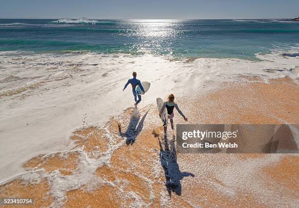 couple of surfers running into the sea. - beach surfer stock pictures, royalty-free photos & images