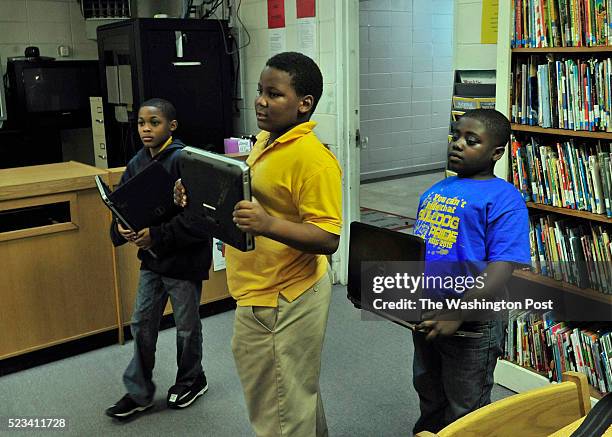 Three students Jarquiese McCaskey, Jaquan Hawkins and Zaylan Randolph hold computers as they enter the school library where they will attempt to do...