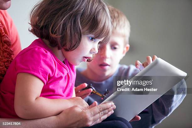 a brother and sister viewing a tablet device with their mother. - famille avec enfants photos et images de collection