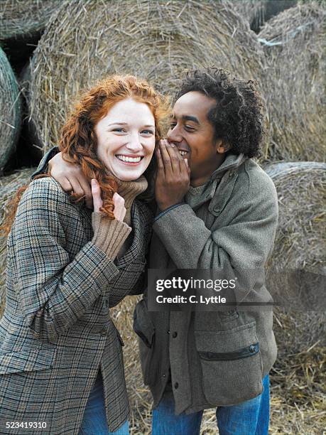 young couple whispering in front of straw bales - woman whisper to man stockfoto's en -beelden