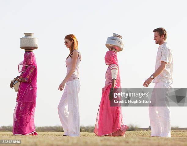 tourist couple walking with two indian women wearing saris and carrying waterjugs - hugh sitton india stock pictures, royalty-free photos & images