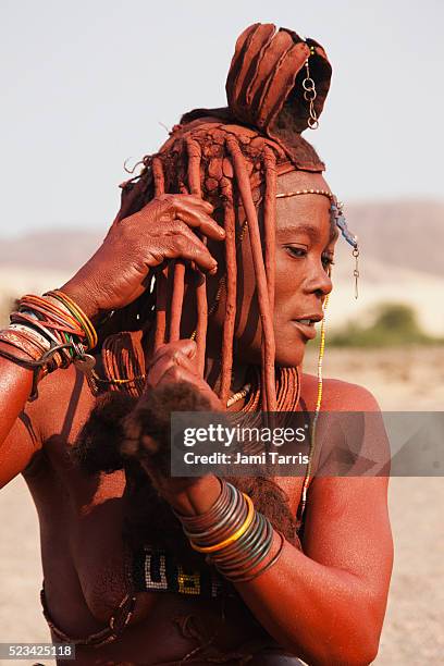 a himba girl mixes ochre and fat to apply to her exposed skin and hair - himba stock-fotos und bilder