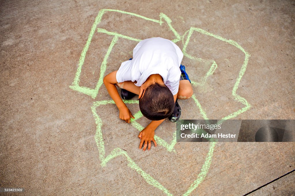 Boy (4-5) drawing recycling symbol on asphalt
