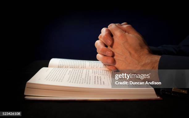 clasped hands on a bible while praying to god - bible stock pictures, royalty-free photos & images