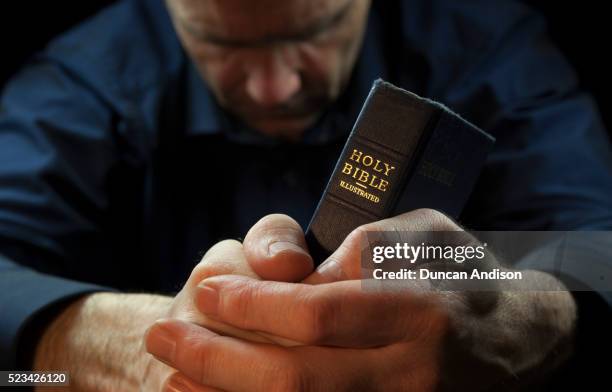a man praying holding a holy bible - biblia fotografías e imágenes de stock