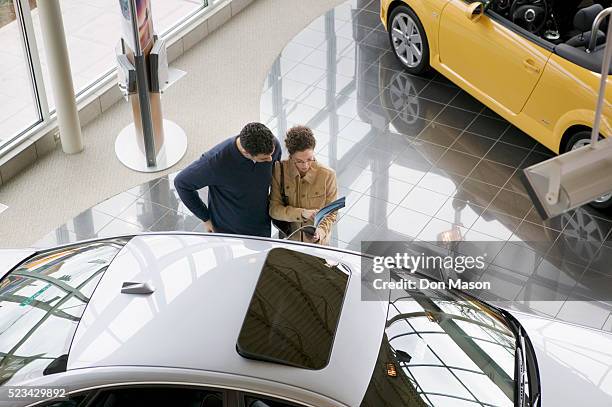 couple reading car information at dealership - salón de coches fotografías e imágenes de stock