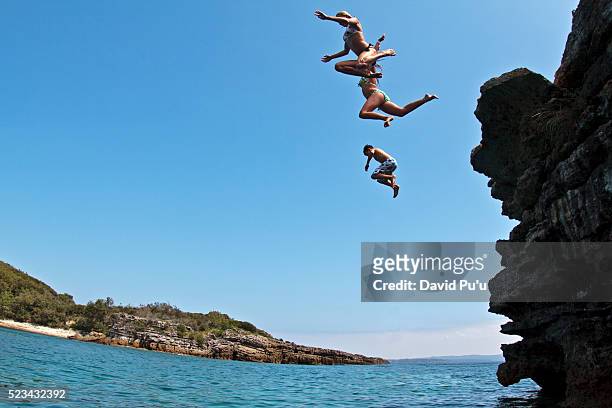 teenagers jumping off low cliff into water - david cliff stock-fotos und bilder