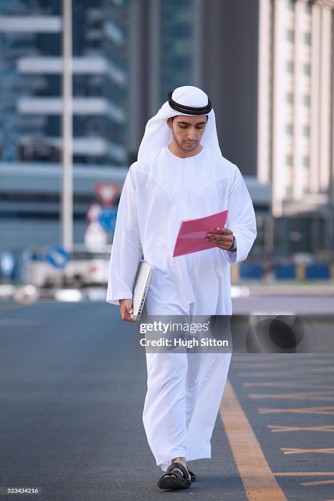 Man wearing traditional clothing reading documents on street