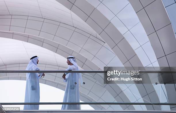 two men wearing traditional clothing talking in front of modern office building - low angle view of two businessmen standing face to face outdoors stock pictures, royalty-free photos & images