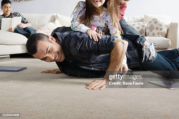 father playing with children in living room - rough housing stock-fotos und bilder