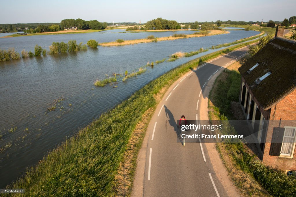Netherlands, Lienden, Woman Cycles On Dyke