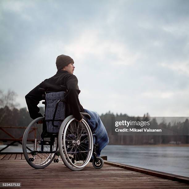 young man in wheelchair on jetty by a lake - silla de ruedas fotografías e imágenes de stock