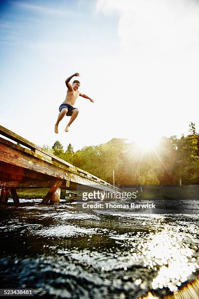 young boy jumping off of dock into lake - taking the plunge 個照片及圖片檔