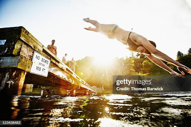 woman in bikini diving off of dock into lake - jumping into lake stock-fotos und bilder