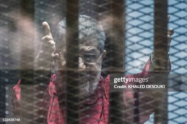 Egypt's ousted Islamist president Mohamed Morsi, wearing a red uniform, gestures from behind the bars during his trial in Cairo at the police academy...