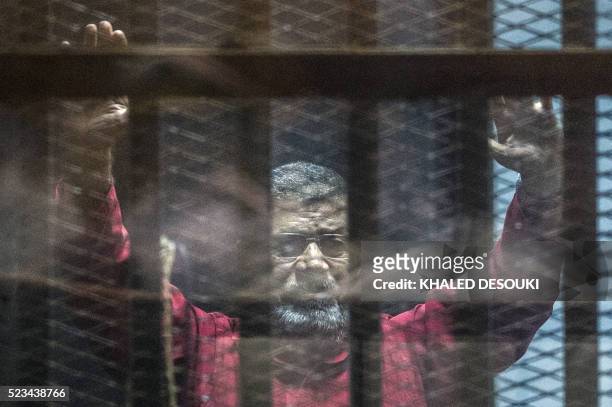 Egypt's ousted Islamist president Mohamed Morsi, wearing a red uniform, gestures from behind the bars during his trial in Cairo at the police academy...