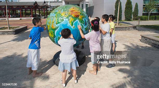 elementary school age children touching a globe of the earth in a playground. - international day eight imagens e fotografias de stock