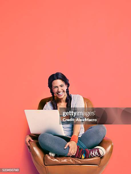 studio portrait of teenage girl (16-17) sitting in armchair with laptop - teen computer stock-fotos und bilder