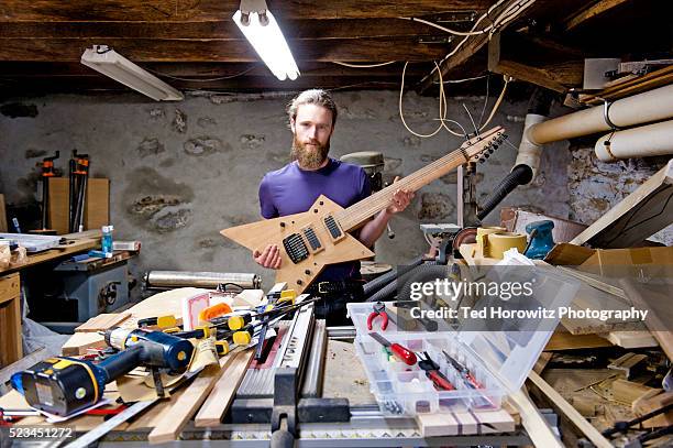 young man holding homemade electric guitar in his basement workshop - hobbies stockfoto's en -beelden