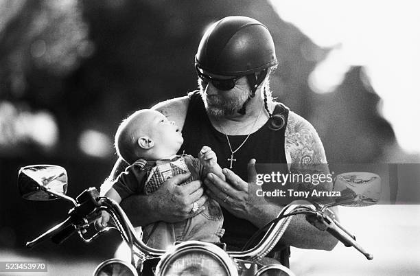 tattooed biker holding a baby - baby sturzhelm stock-fotos und bilder