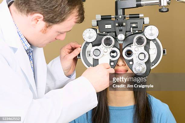optometrist examining patient with phoropter - réfracteur photos et images de collection